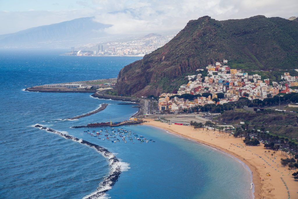 Aerial shot of Tenerife beach in the Canary Islands with buildings, mountains, and blue sea