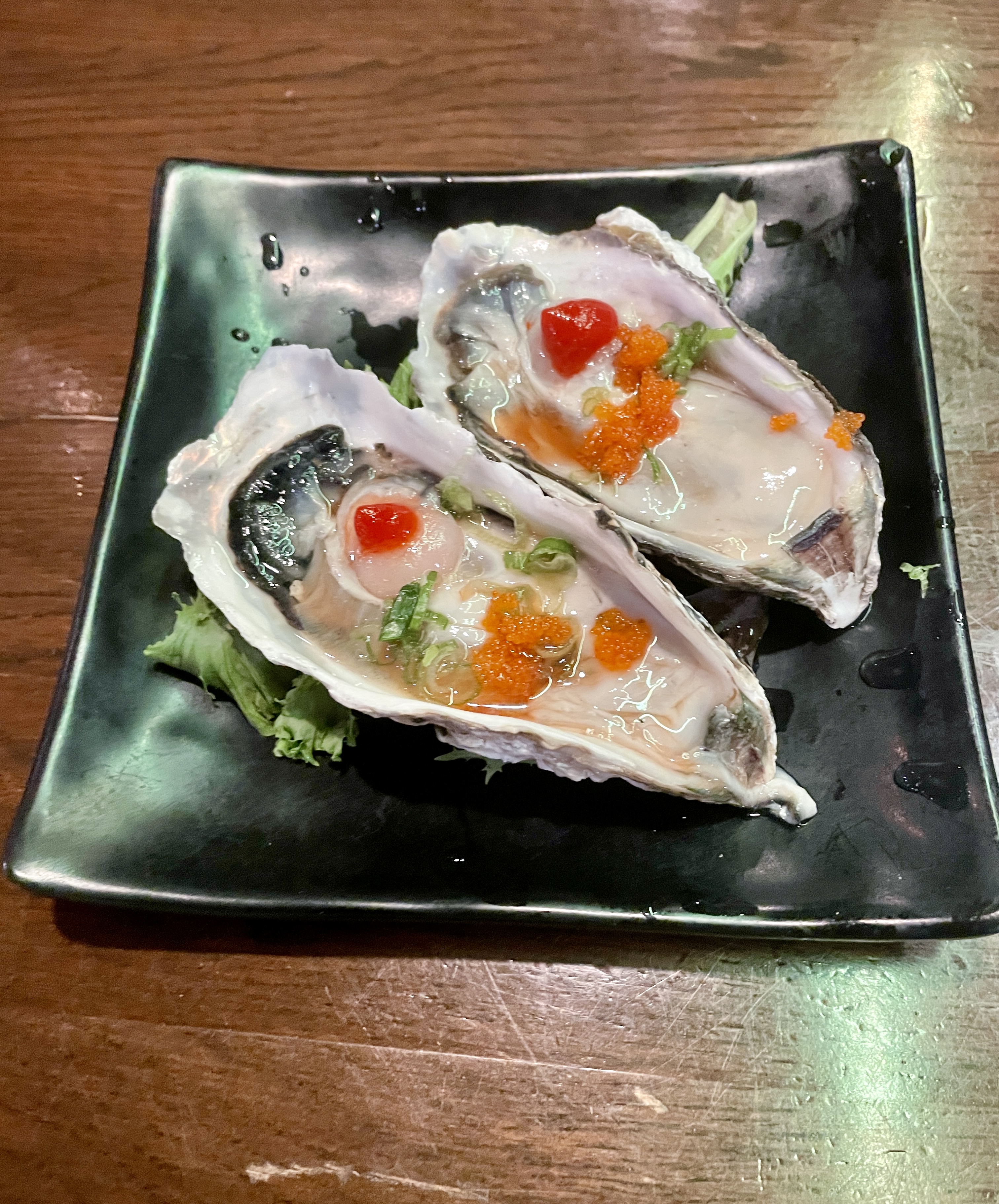 Two fresh oysters in the shell on a black plate on a brown table