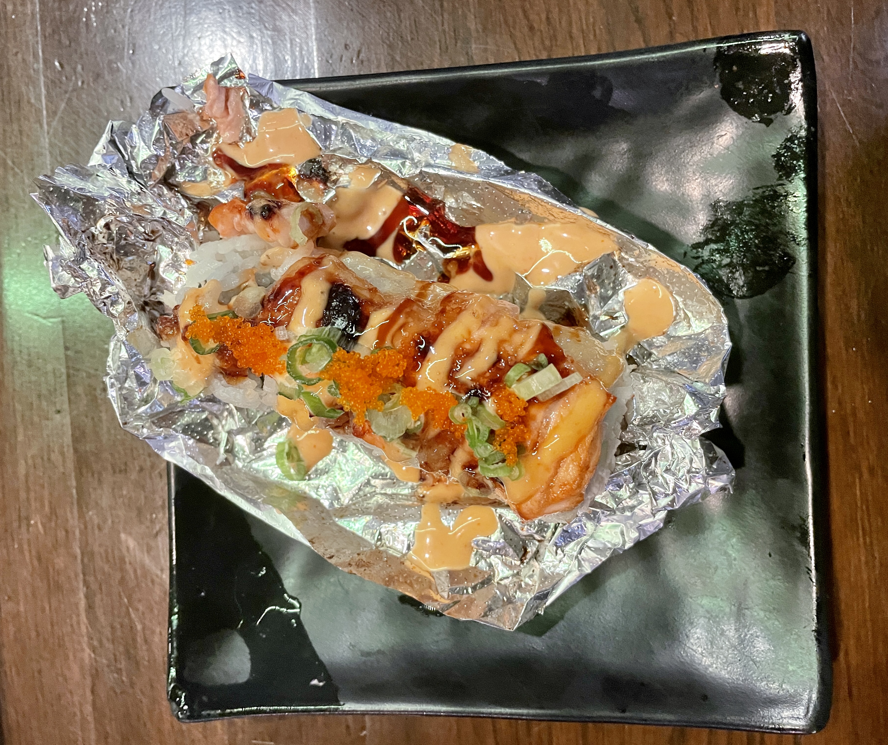 Baked salmon roll in foil on black plate on a brown table